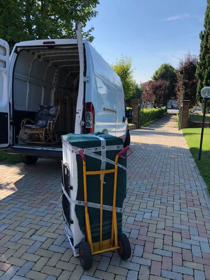Carrello a due ruote con un mobile protetto da coperta verde davanti al furgone aperto